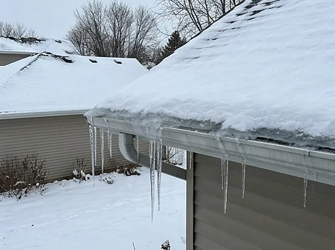 Ice dam and icicles on a snowy Minnesota roof edge and gutter