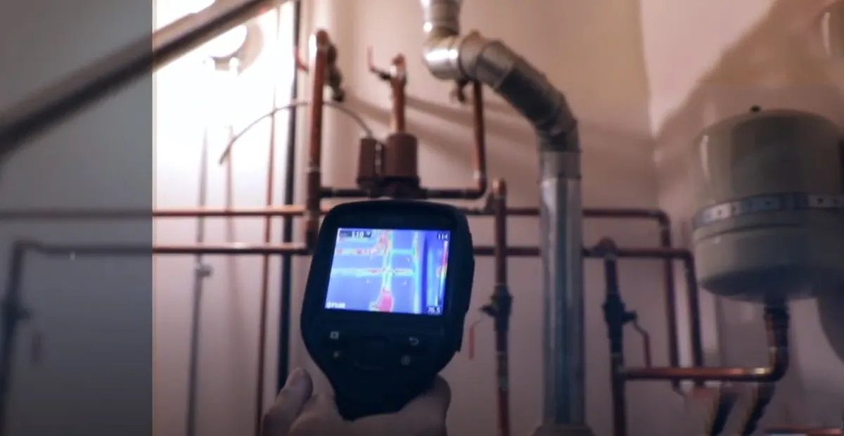 A thermal camera pointed at basement pipes, showing a heat image on its screen